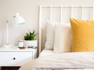 White nightstand with white night lamp and decor items next to bed with pillows and white headboard closeup